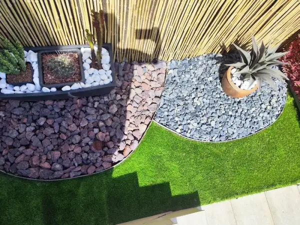 Parterres curvos de piedra volcánica y grava gris sobre césped artificial